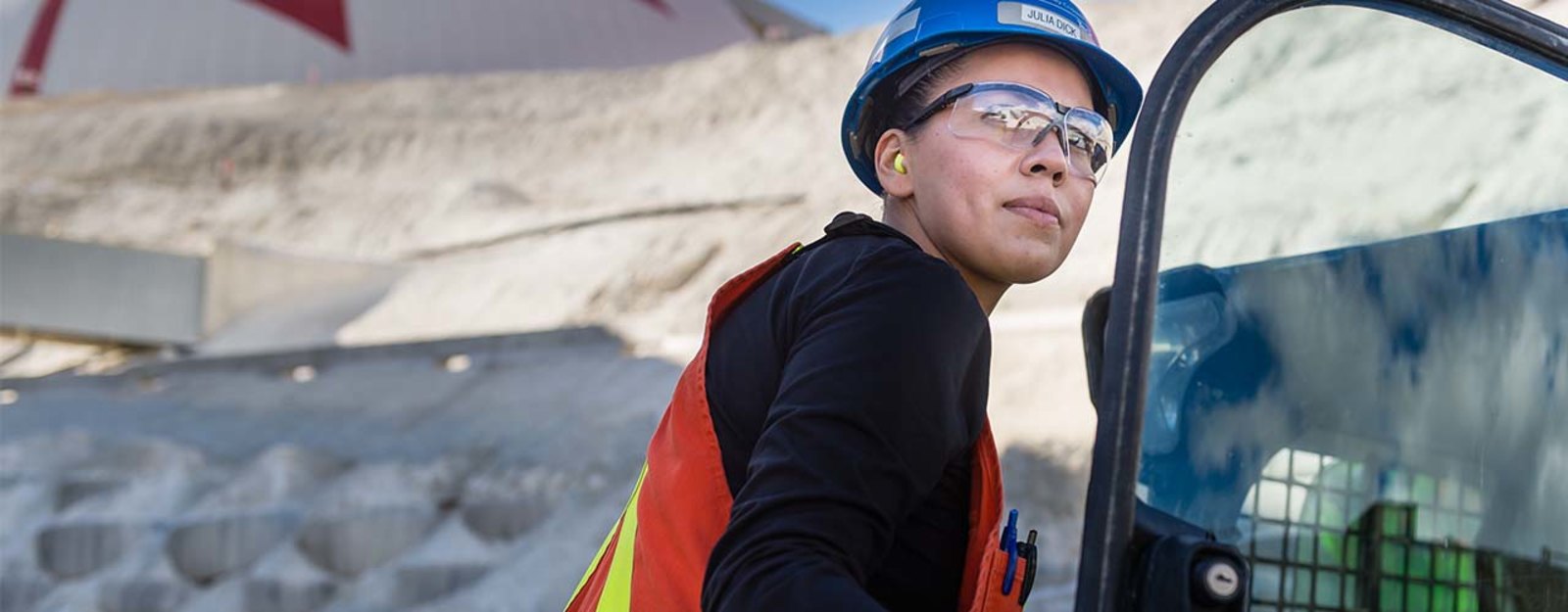 Worker in safety gear and hard hat operates machinery at a construction site.